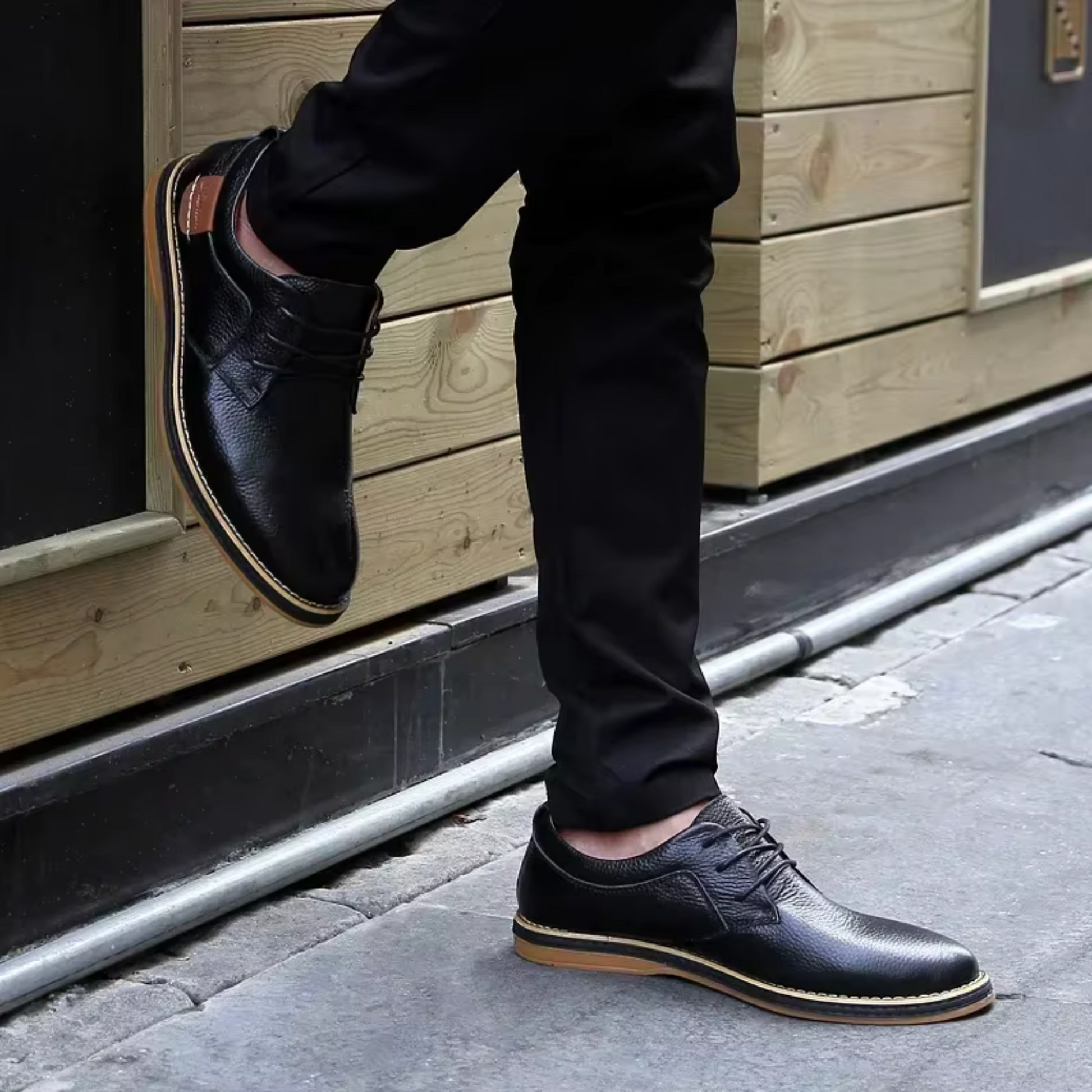 Black genuine leather men's moccasins paired with casual black pants on a street pavement.
